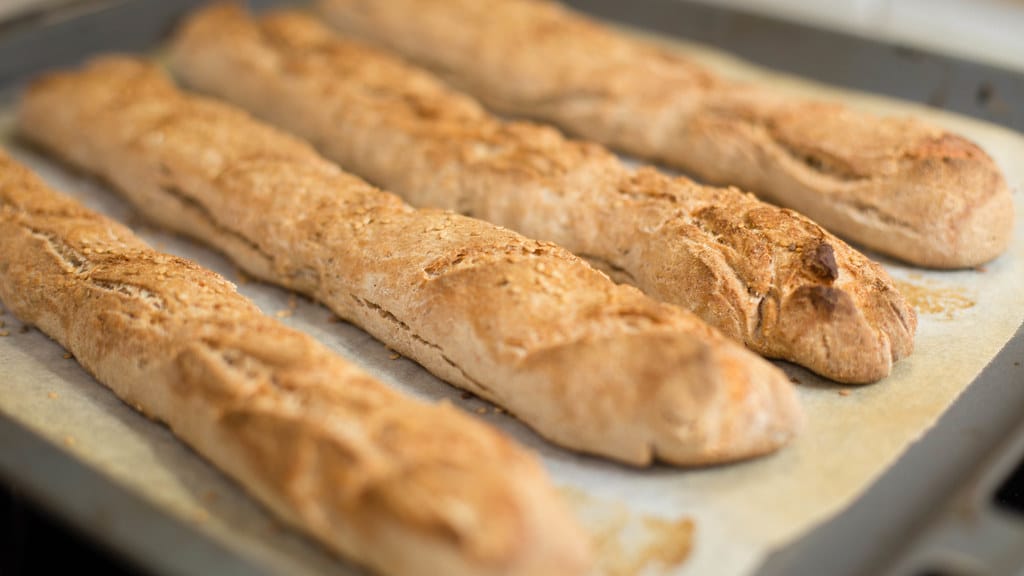 Freshly baked golden baguettes cooling on a baking tray at an artisan bakery
