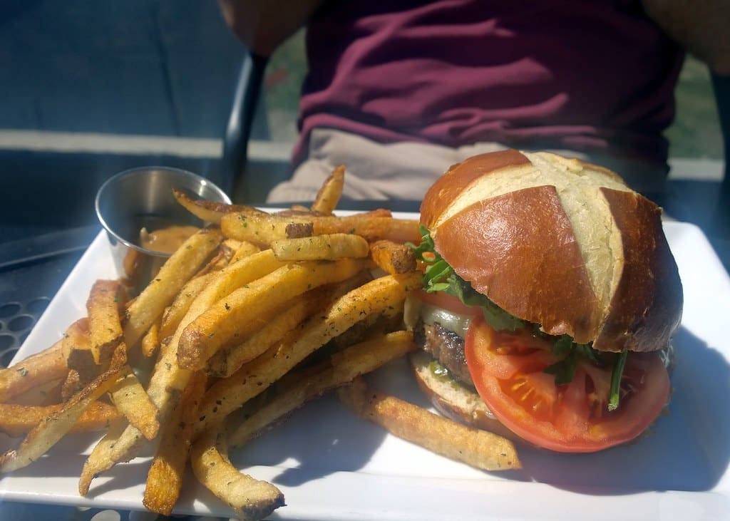 Burger on a pretzel bun with hand-cut fries served on a sunny outdoor patio table