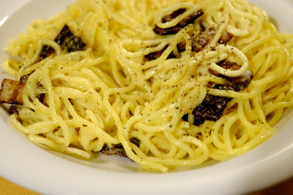 A bowl of fresh spaghetti carbonara topped with crispy cured pork and cracked black pepper