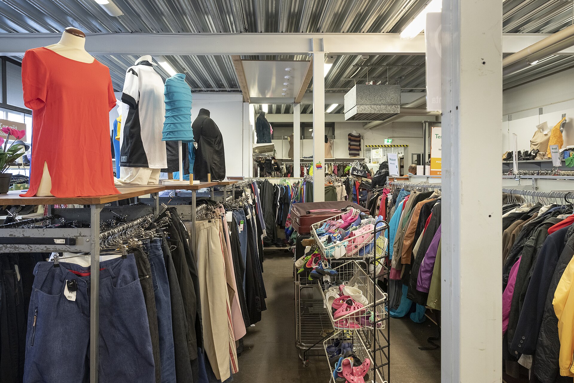 Rails of pre-loved jeans, coats and colourful tops on hangers inside a secondhand clothing shop