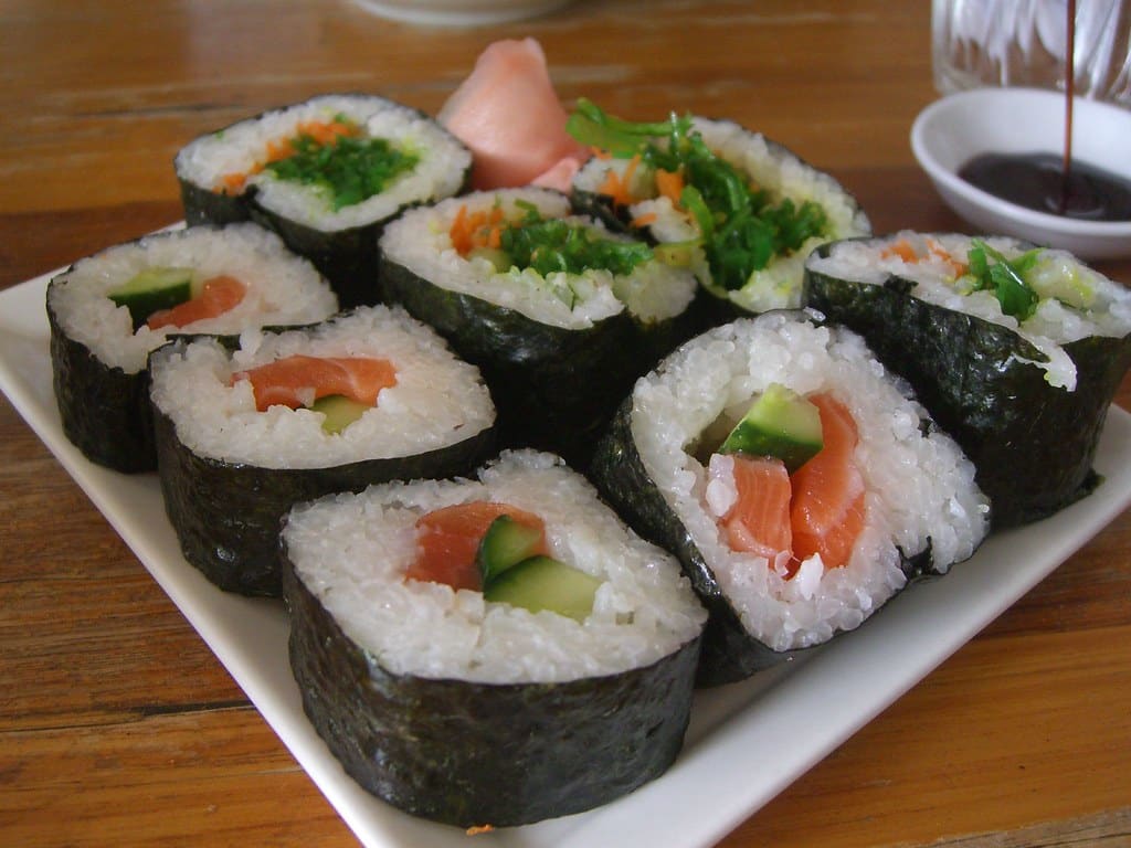 A plate of fresh salmon and cucumber sushi rolls with pickled ginger and a dish of soy sauce