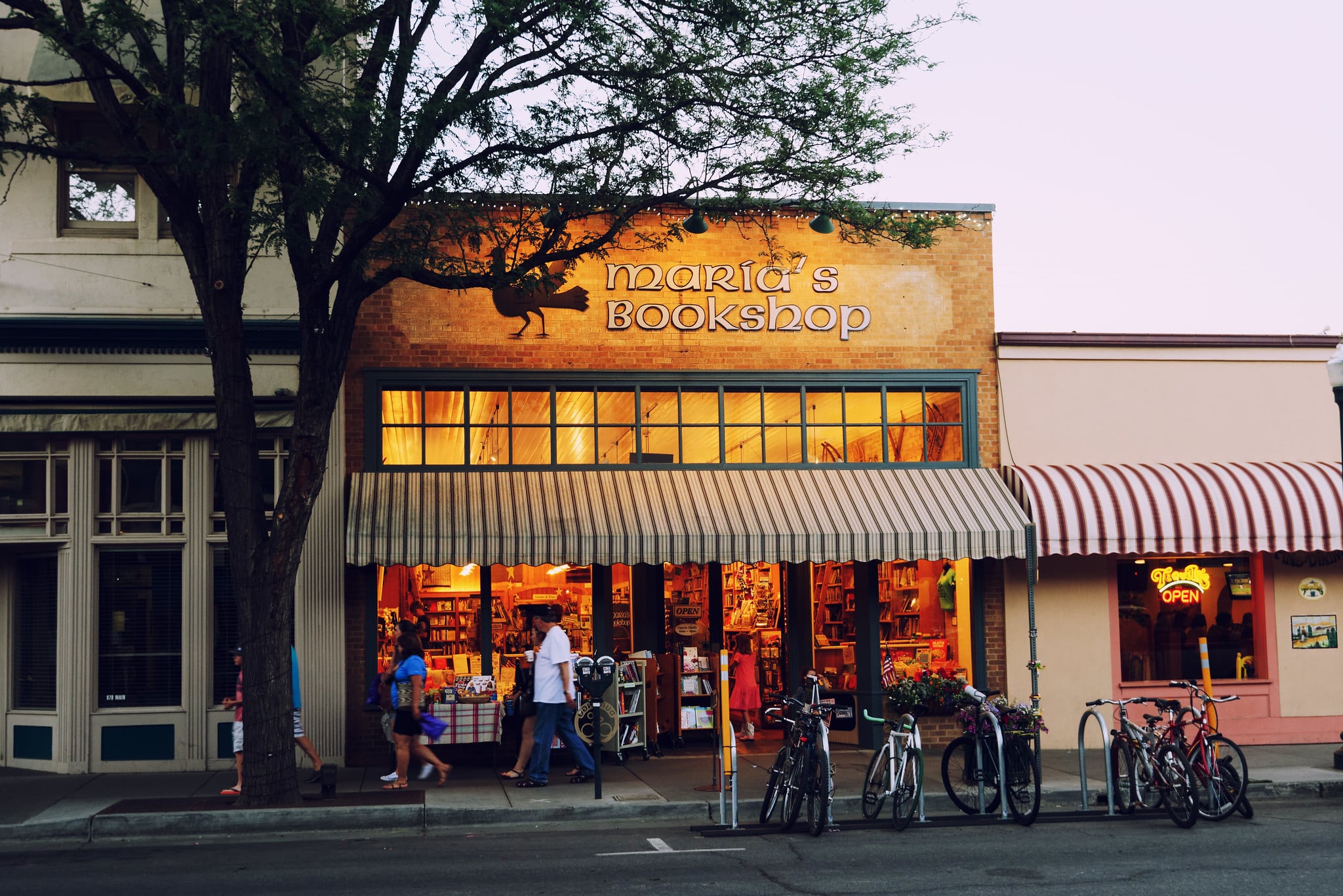 Maria's Bookshop storefront on Main Avenue in Durango at dusk, with its striped awning, glowing windows and bikes parked outside