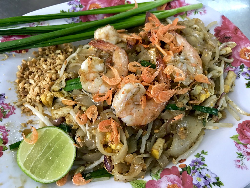 Plate of shrimp pad thai with crushed peanuts, spring onions and a wedge of lime