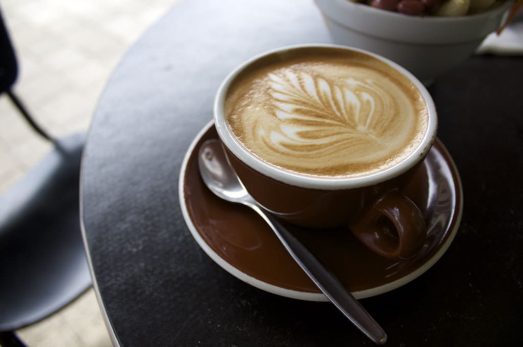 A flat white with leaf-pattern latte art on a café table