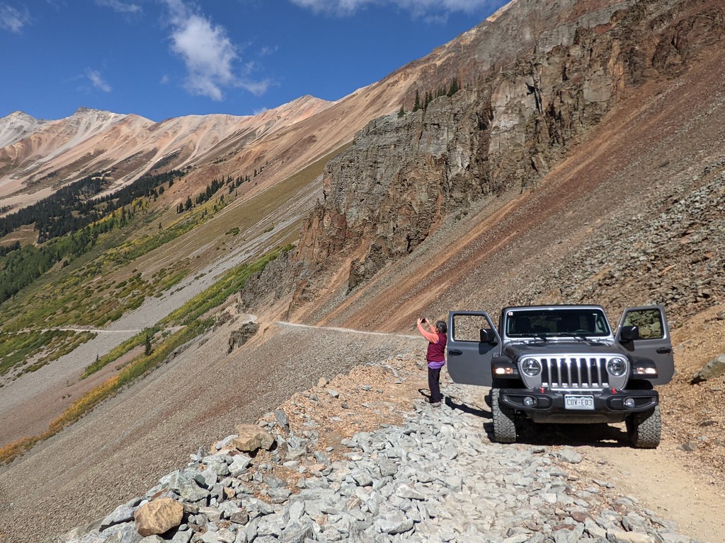Jeep Wrangler parked on the rocky Ophir Pass road with colourful San Juan mountain slopes and blue sky behind
