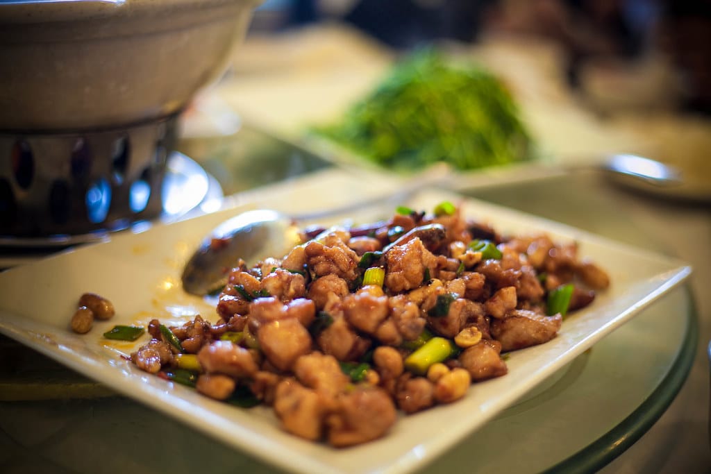 A plate of Kung Pao chicken with peanuts and spring onions on a restaurant table