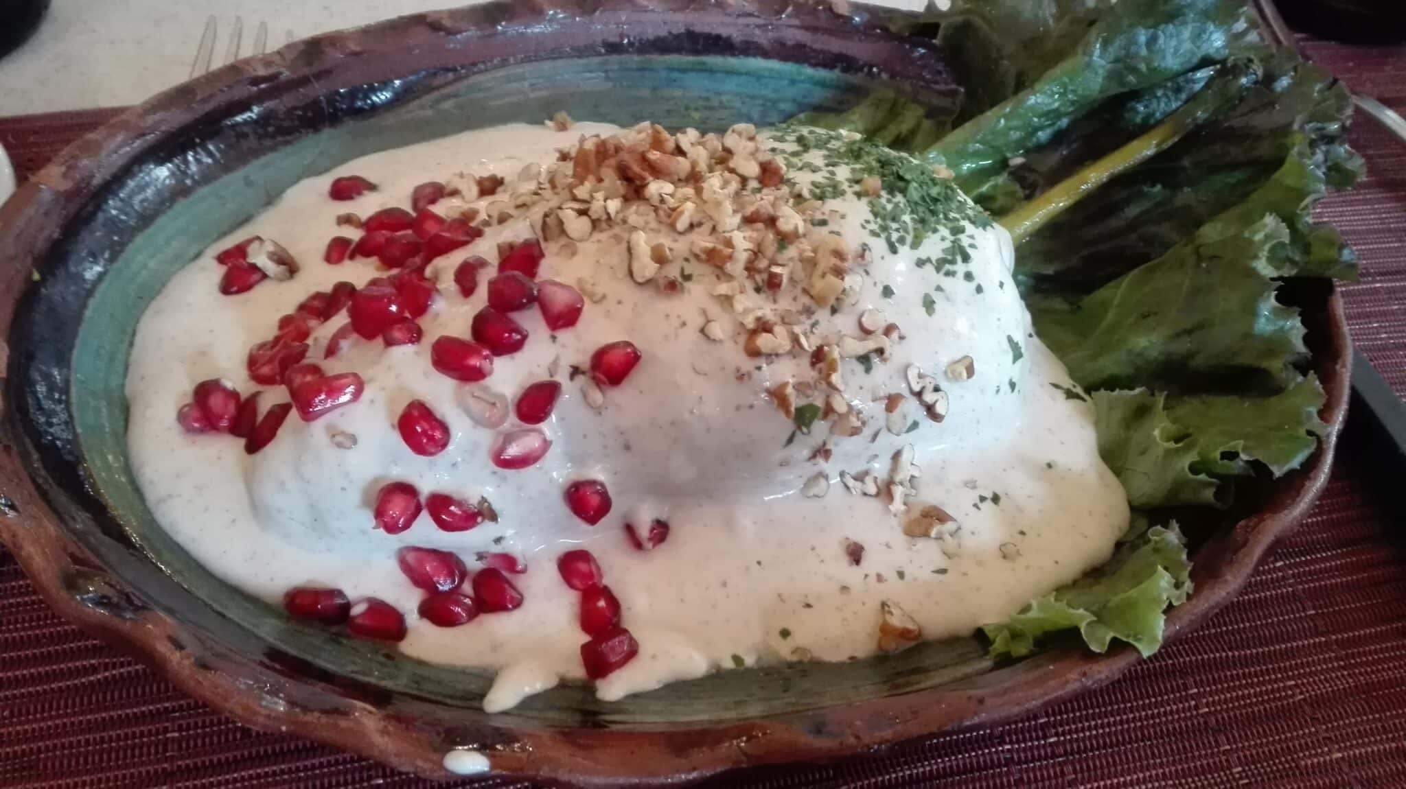 Chile en nogada topped with creamy walnut sauce, pomegranate seeds and chopped nuts, served in a rustic clay dish