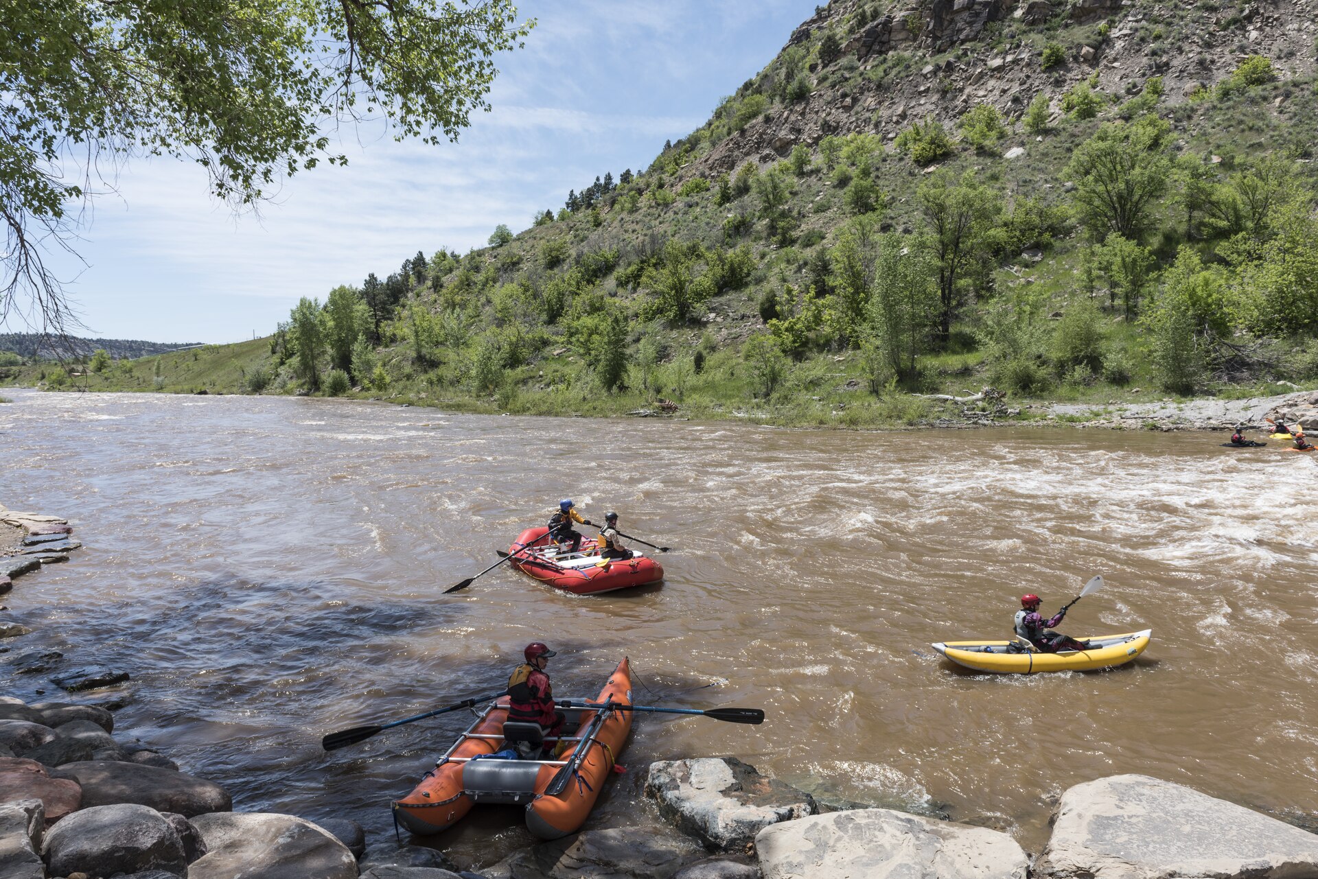Rafts and an inflatable kayak on the rushing Animas River below a green hillside near Durango