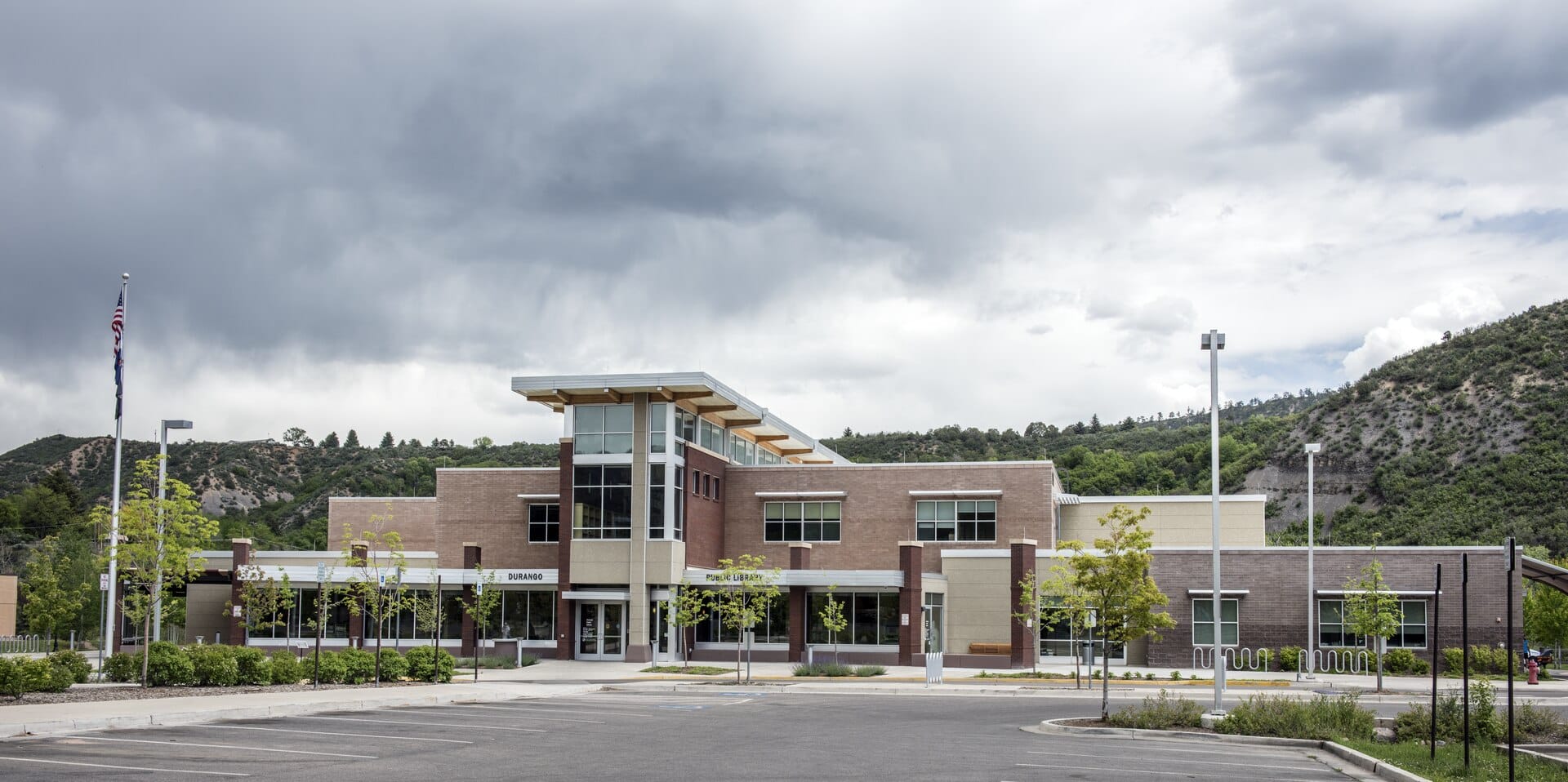 The modern brick Durango Public Library building with green hills and cloudy skies behind it